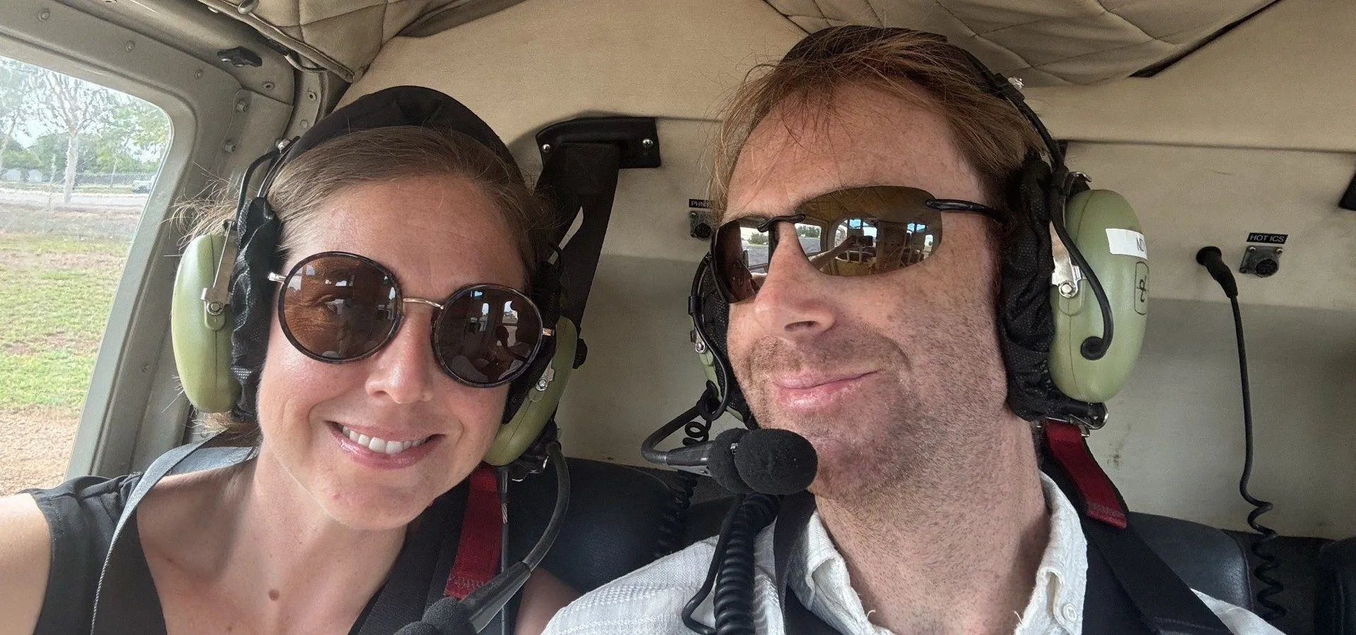 Jordan and Cindy, headsets on, in the cabin of a helicopter.